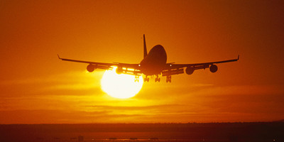 Air New Zealand's Boeing 747-400 aircraft flying over a runway with the sun behind it.