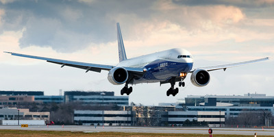 Boeing 777 aircraft flying over a runway.